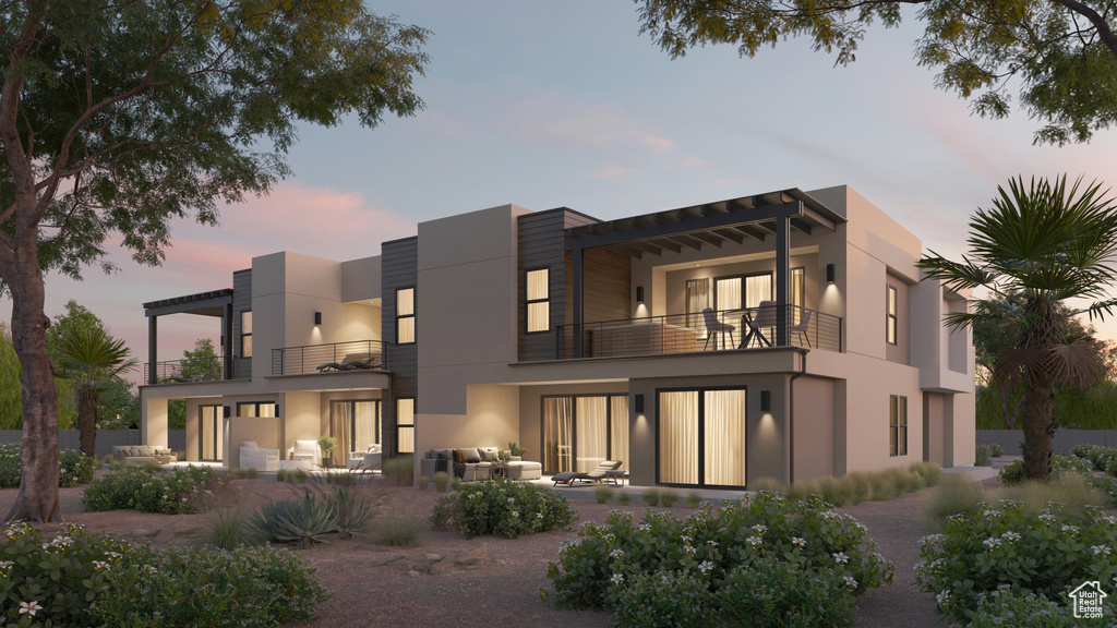 Back of house at dusk with stucco siding, an outdoor living space, a patio area, and a balcony