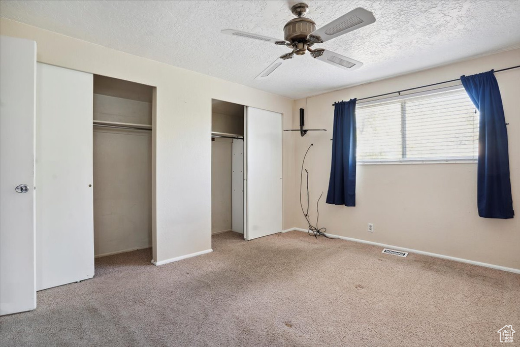 Unfurnished bedroom featuring a textured ceiling, visible vents, baseboards, multiple closets, and carpet