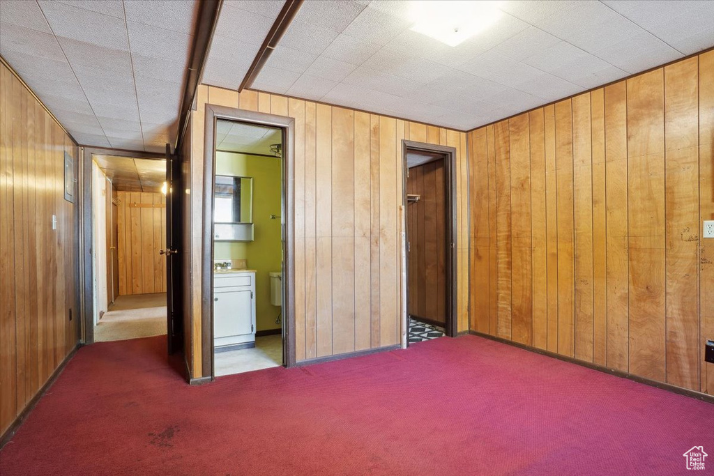Unfurnished bedroom with carpet flooring, wood walls, and ensuite bath