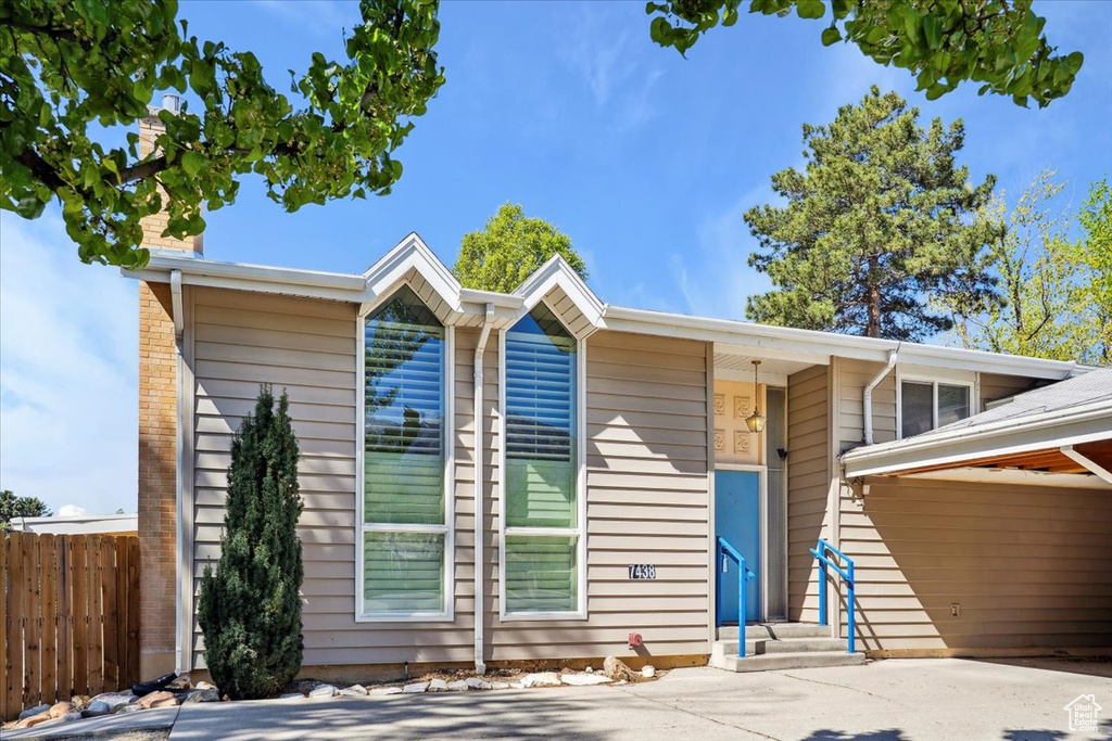 View of front of house featuring concrete driveway, fence, and a chimney