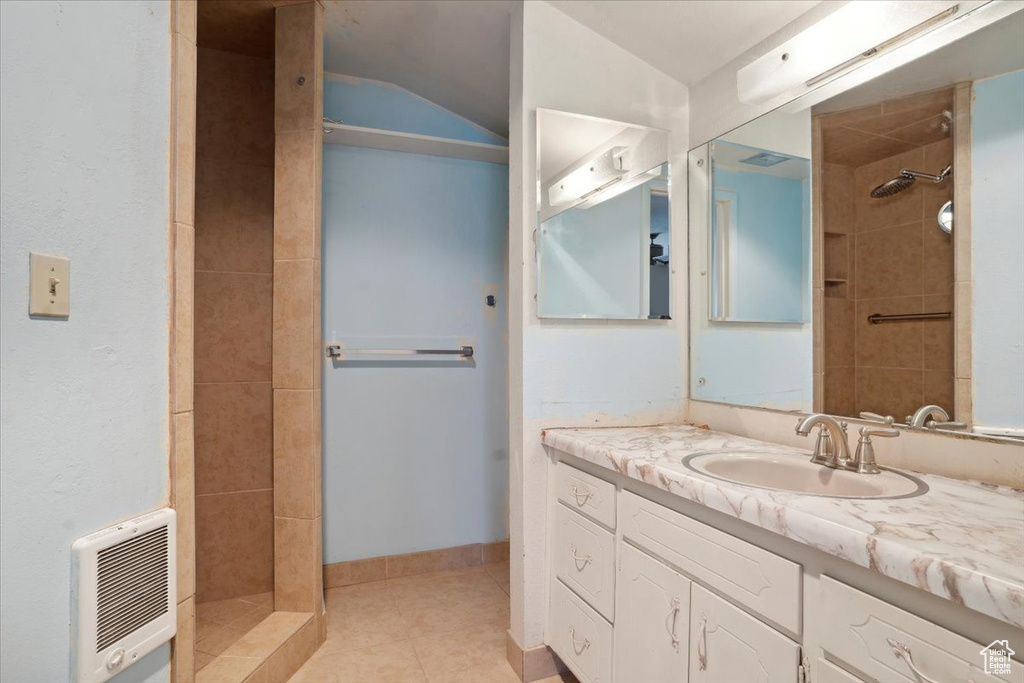 Bathroom with vaulted ceiling, tile patterned floors, vanity, heating unit, and tiled shower
