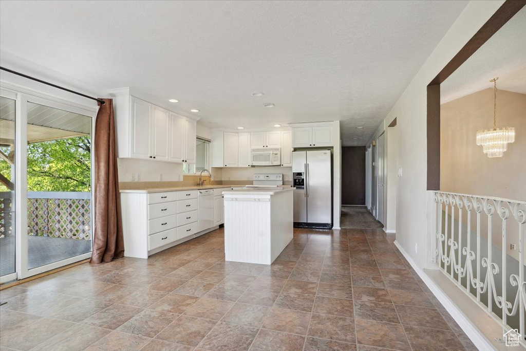 Kitchen featuring light countertops, stone finish floor, a kitchen island, and white appliances