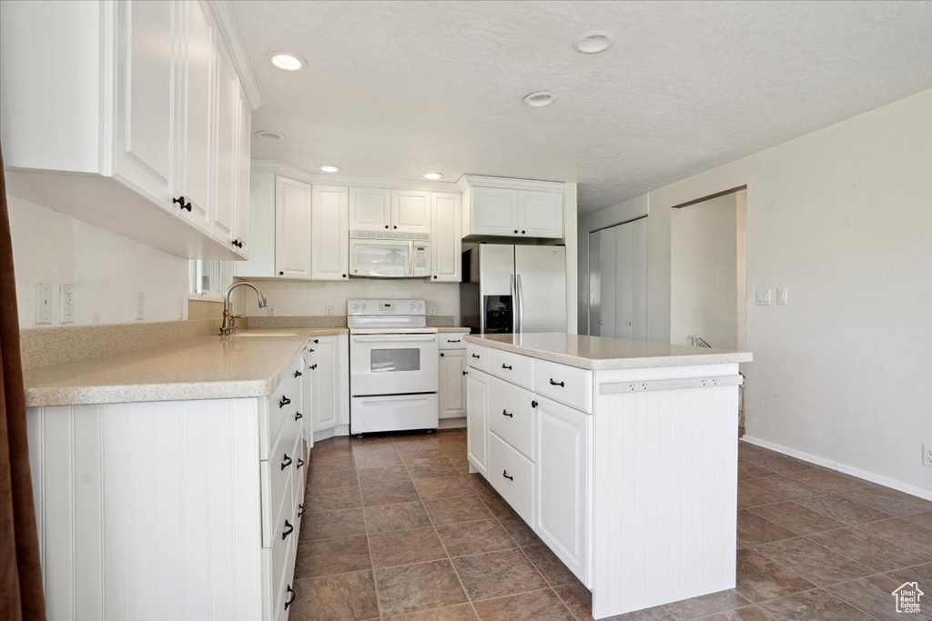 Kitchen with white cabinetry, a sink, light countertops, recessed lighting, and white appliances