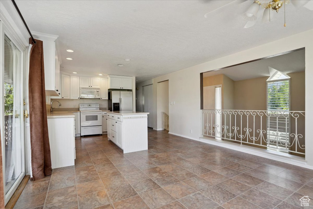 Kitchen with a center island, light countertops, baseboards, white cabinets, and white appliances