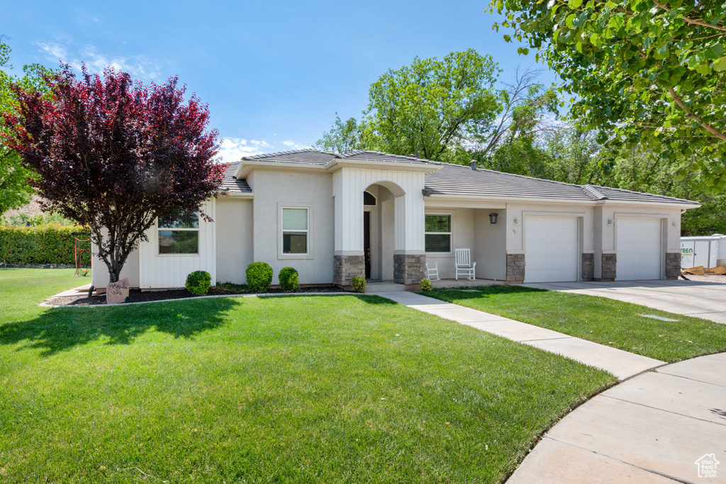 Single story home with stone siding, a garage, a front yard, concrete driveway, and a tiled roof