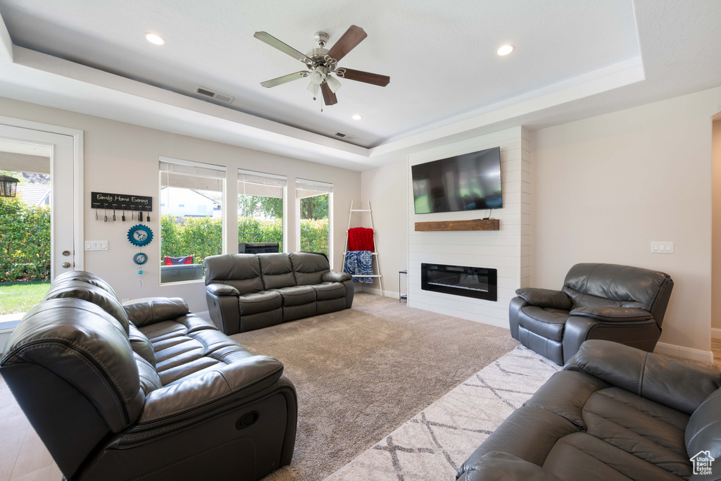 Carpeted living room with a ceiling fan, visible vents, a fireplace, a tray ceiling, and recessed lighting