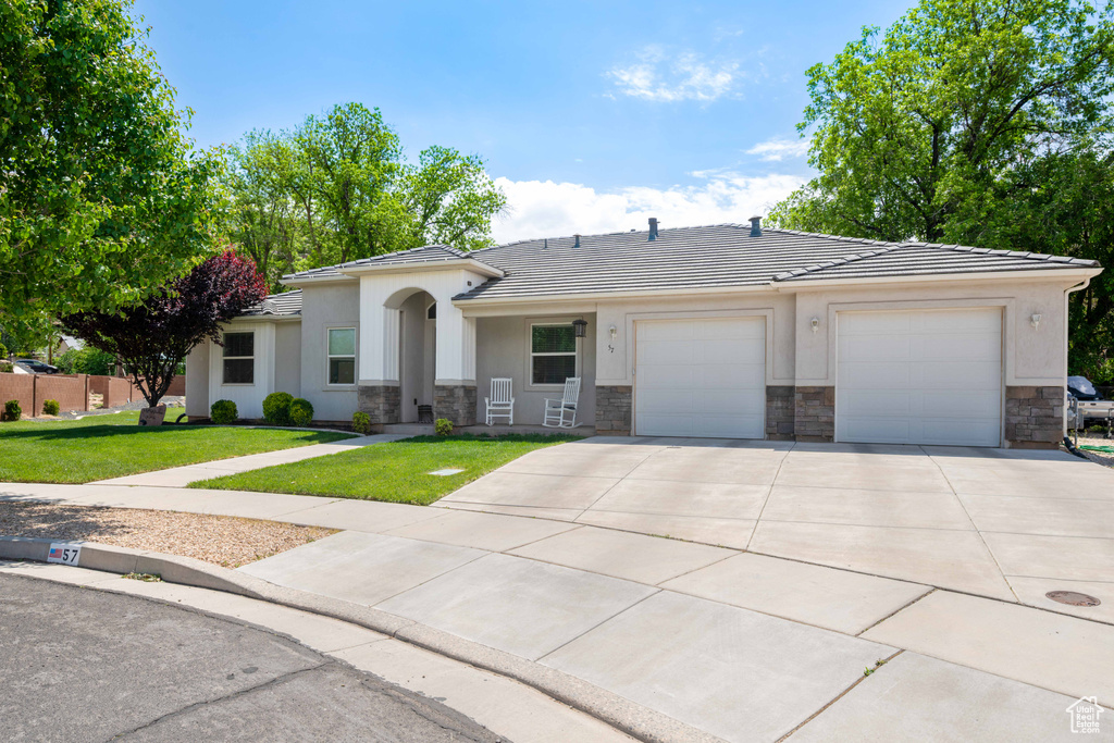 Ranch-style home with driveway, a tile roof, a garage, a front lawn, and stone siding