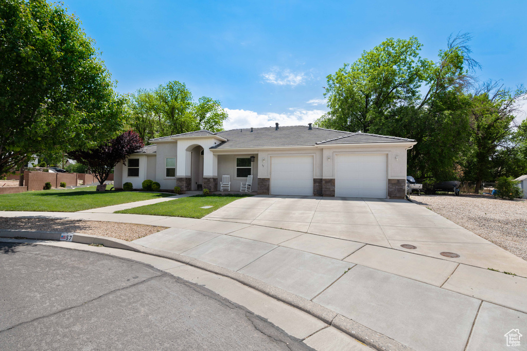 Single story home with driveway, a front yard, a garage, stone siding, and stucco siding