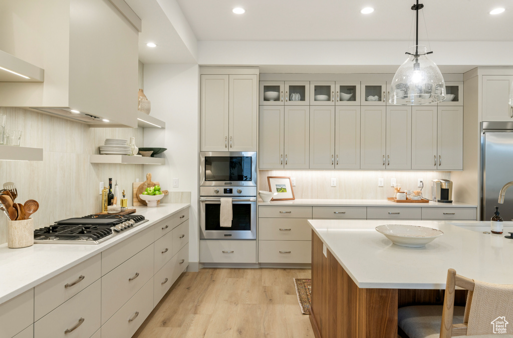 Kitchen with light wood-style floors, built in appliances, light countertops, recessed lighting, and tasteful backsplash