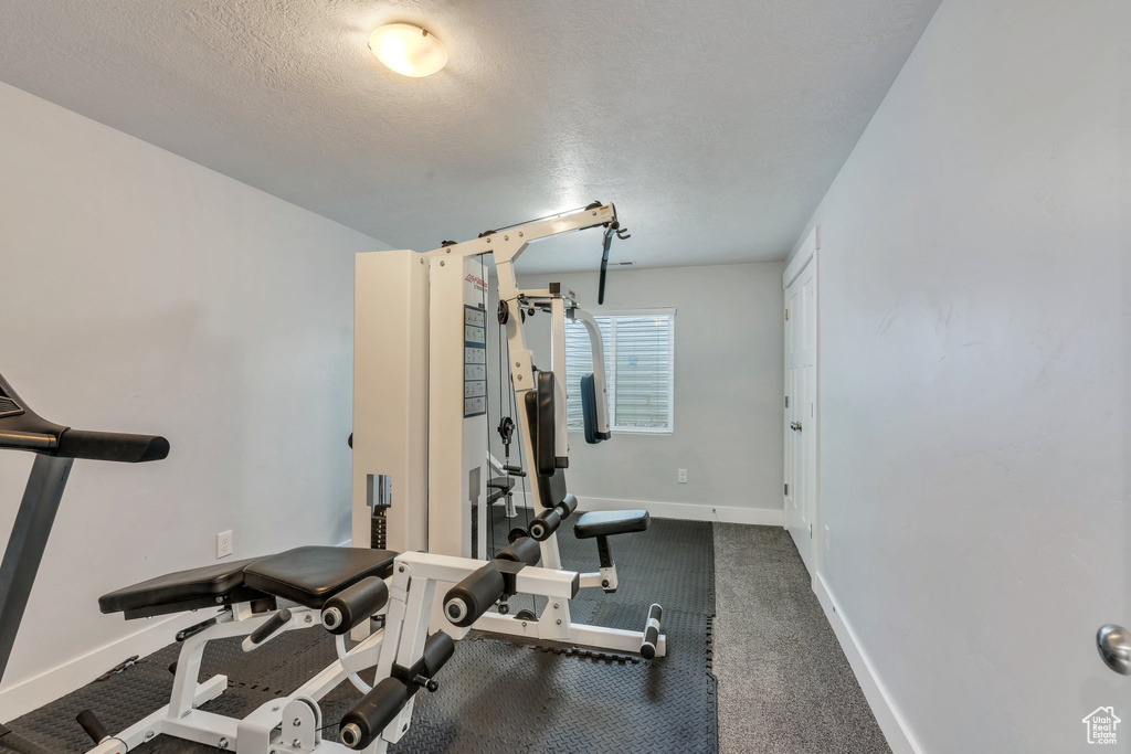 Exercise room with baseboards, a textured ceiling, and carpet