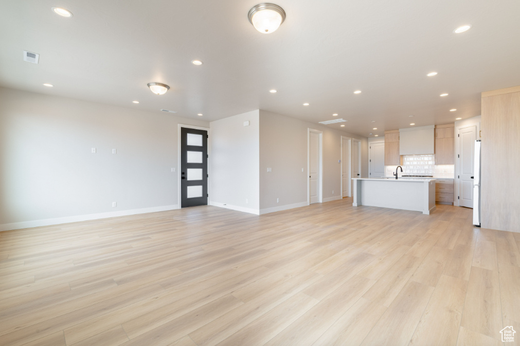 Unfurnished living room featuring visible vents, a sink, baseboards, light wood finished floors, and recessed lighting