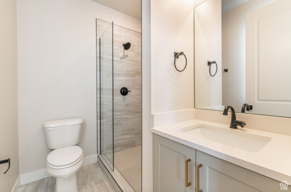 Full bath with toilet, baseboards, tiled shower, and vanity