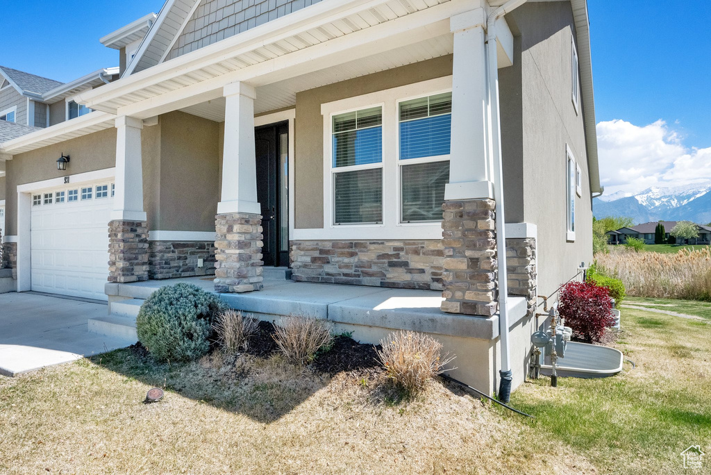 Exterior space featuring covered porch, an attached garage, driveway, and stone siding
