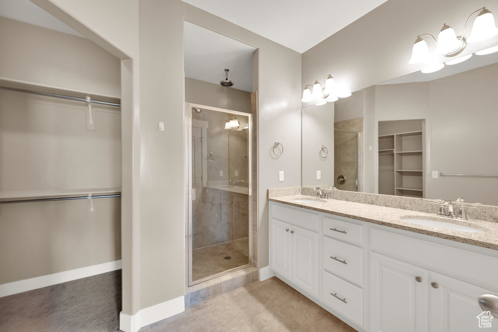 Full bathroom with double vanity, a walk in closet, a sink, and a stall shower