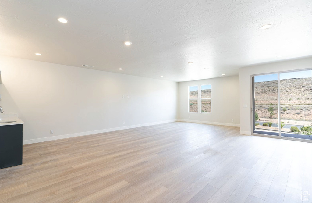 Unfurnished living room featuring light wood-style floors, baseboards, recessed lighting, and a wealth of natural light