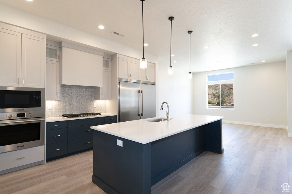Kitchen with a sink, light wood-style floors, built in appliances, tasteful backsplash, and visible vents
