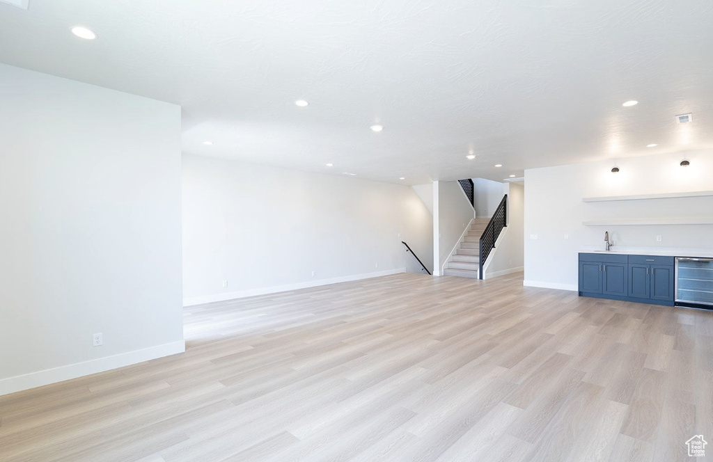 Unfurnished living room featuring indoor wet bar, beverage cooler, stairway, a sink, and light wood finished floors