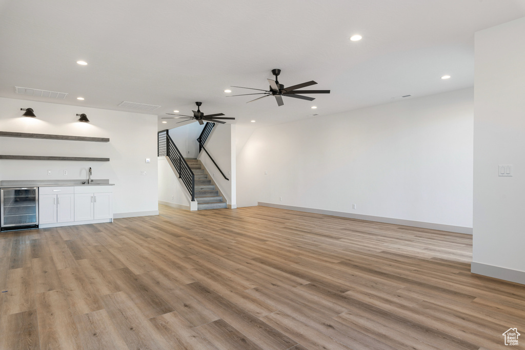Unfurnished living room featuring wine cooler, stairway, indoor wet bar, and recessed lighting