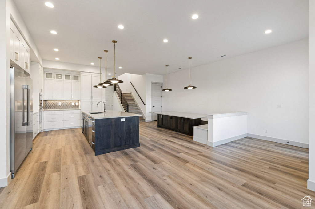Kitchen with a sink, light wood-style flooring, white cabinetry, a spacious island, and high quality fridge