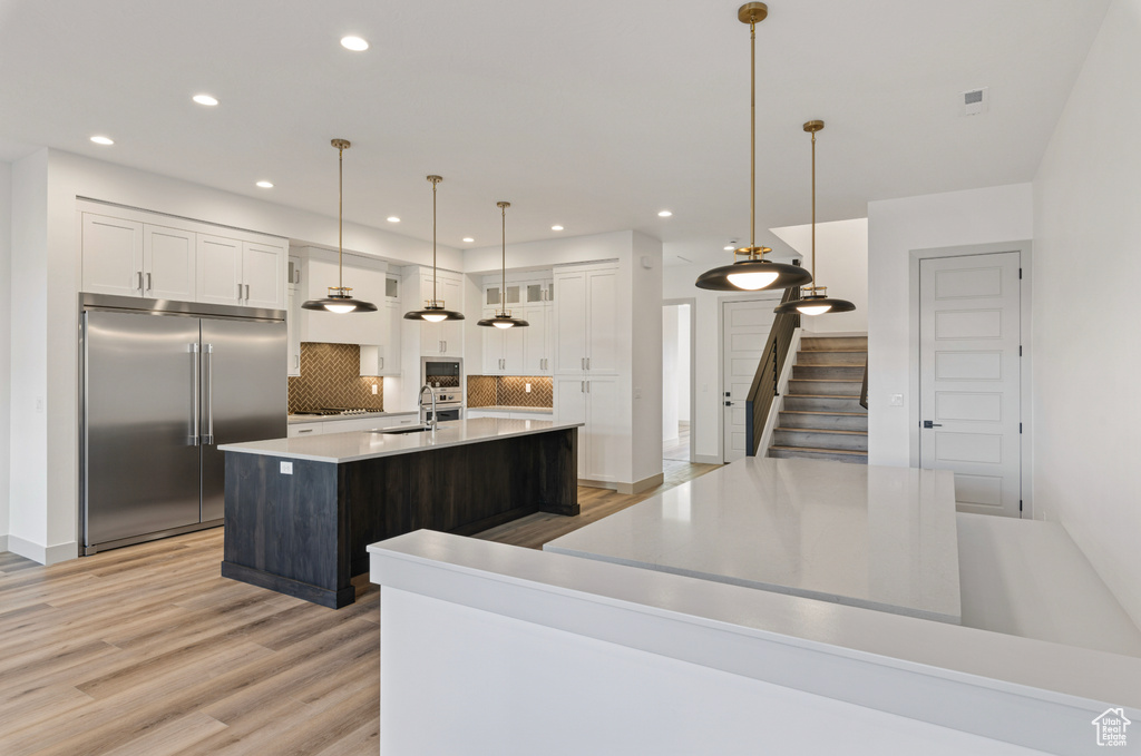 Kitchen with built in appliances, backsplash, white cabinetry, and a kitchen island with sink