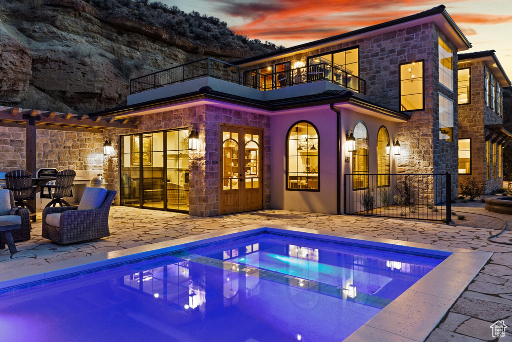 Rear view of house with a patio area, an outdoor pool, a balcony, and stone siding
