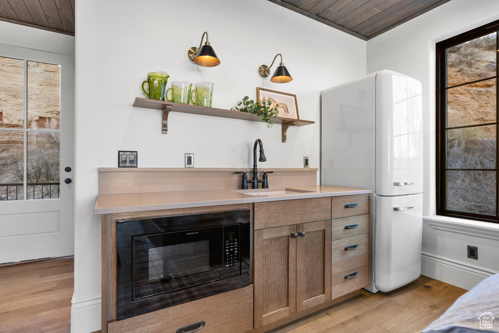 Interior space with a sink, freestanding refrigerator, black microwave, and wooden ceiling