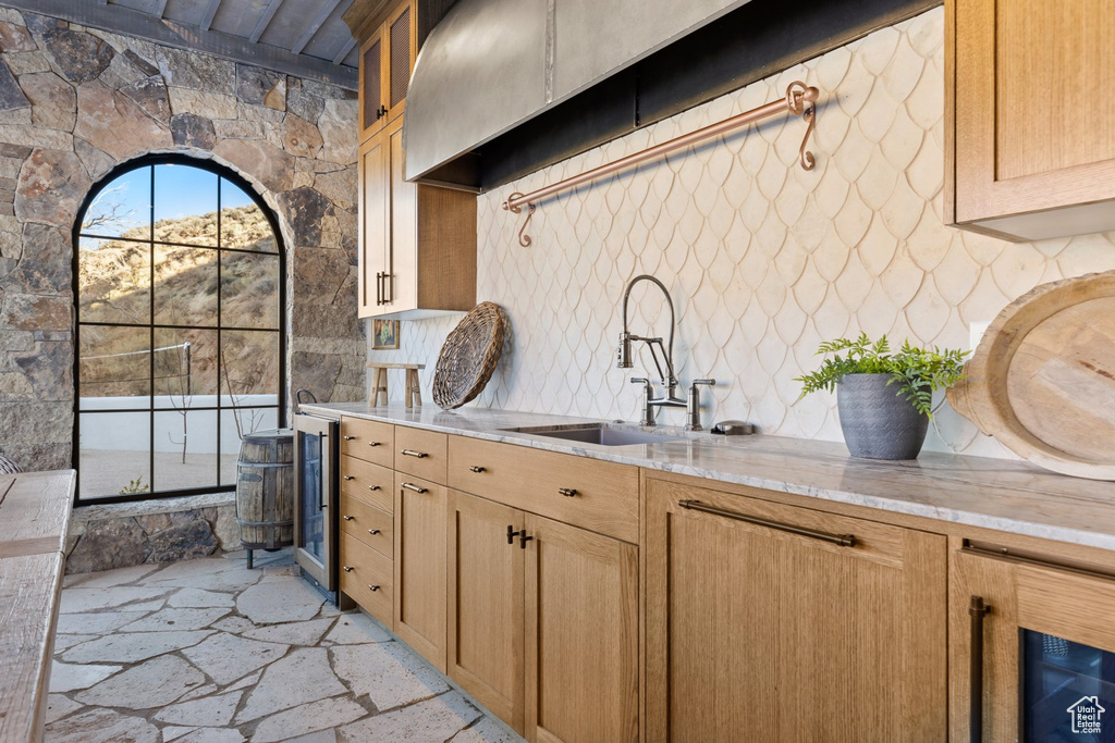 Kitchen with stone floors, glass insert cabinets, beverage cooler, light stone countertops, and a sink