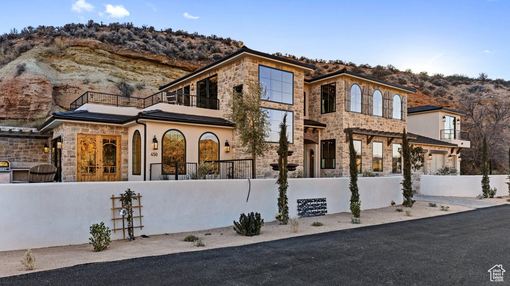 View of front of home with french doors, a fenced front yard, a mountain view, a balcony, and stone siding