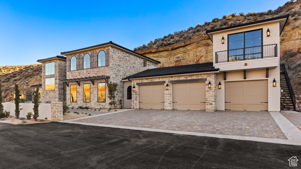 View of front of property with stone siding, stucco siding, a mountain view, decorative driveway, and a balcony