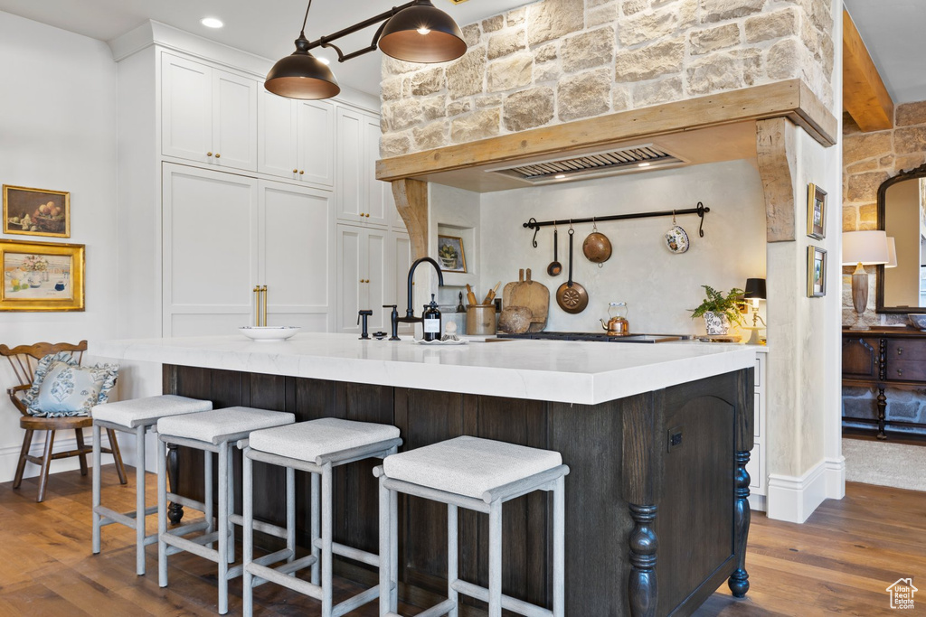 Kitchen with a breakfast bar, dark wood-style floors, light countertops, white cabinets, and a sink