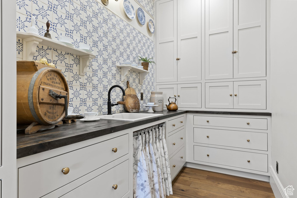Kitchen featuring a sink, open shelves, wood finished floors, and white cabinetry