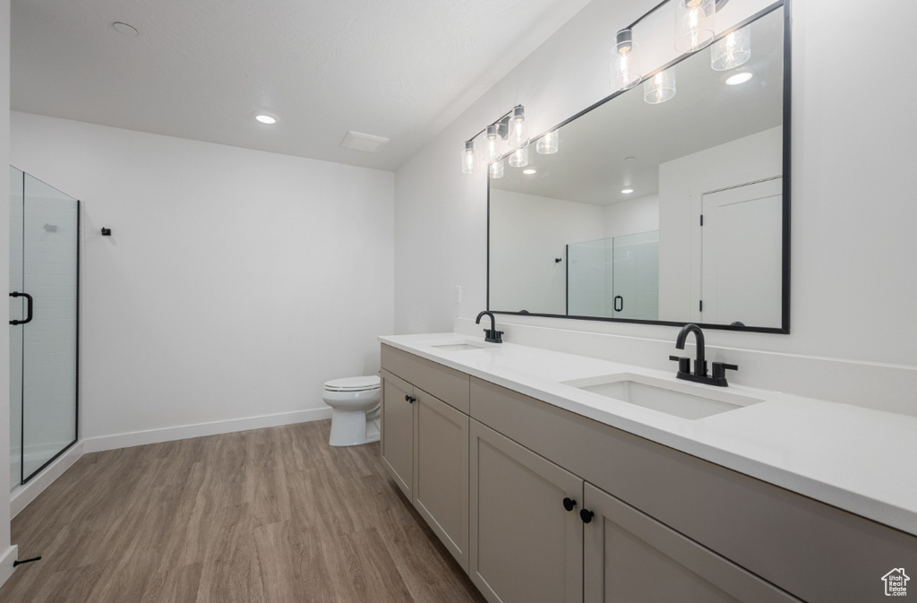 Full bath featuring wood finished floors, a shower stall, double vanity, toilet, and baseboards