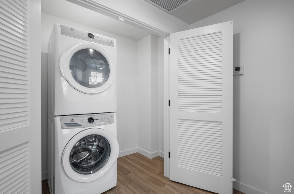 Laundry room featuring stacked washing machine and dryer, baseboards, and wood finished floors