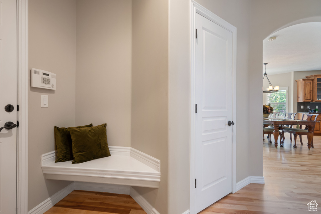 Mudroom featuring light wood-type flooring, arched walkways, baseboards, and an inviting chandelier