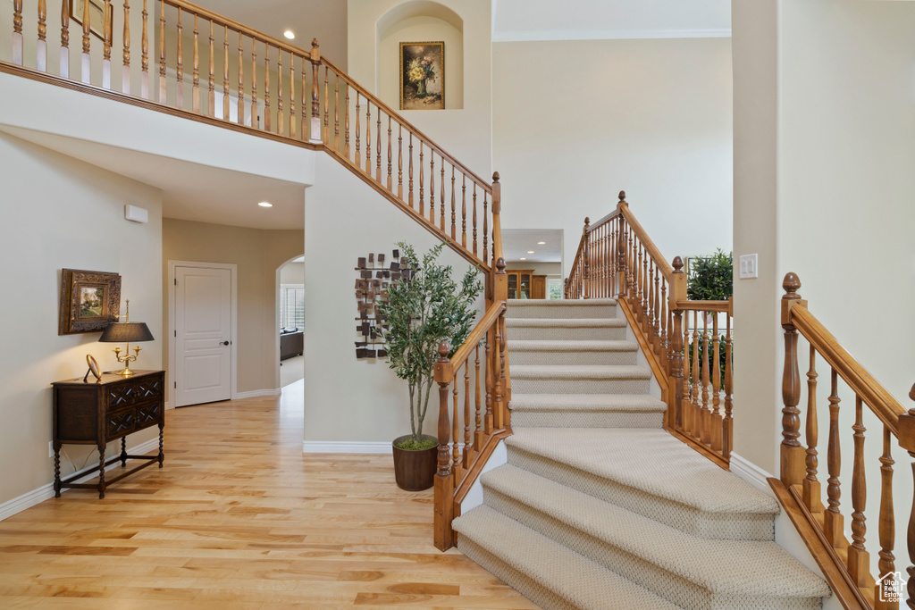 Stairway with wood finished floors, recessed lighting, arched walkways, a high ceiling, and baseboards