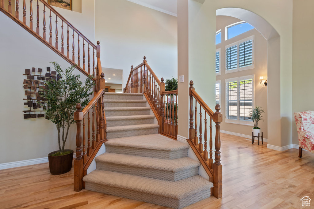 Staircase featuring baseboards, arched walkways, a towering ceiling, and wood finished floors