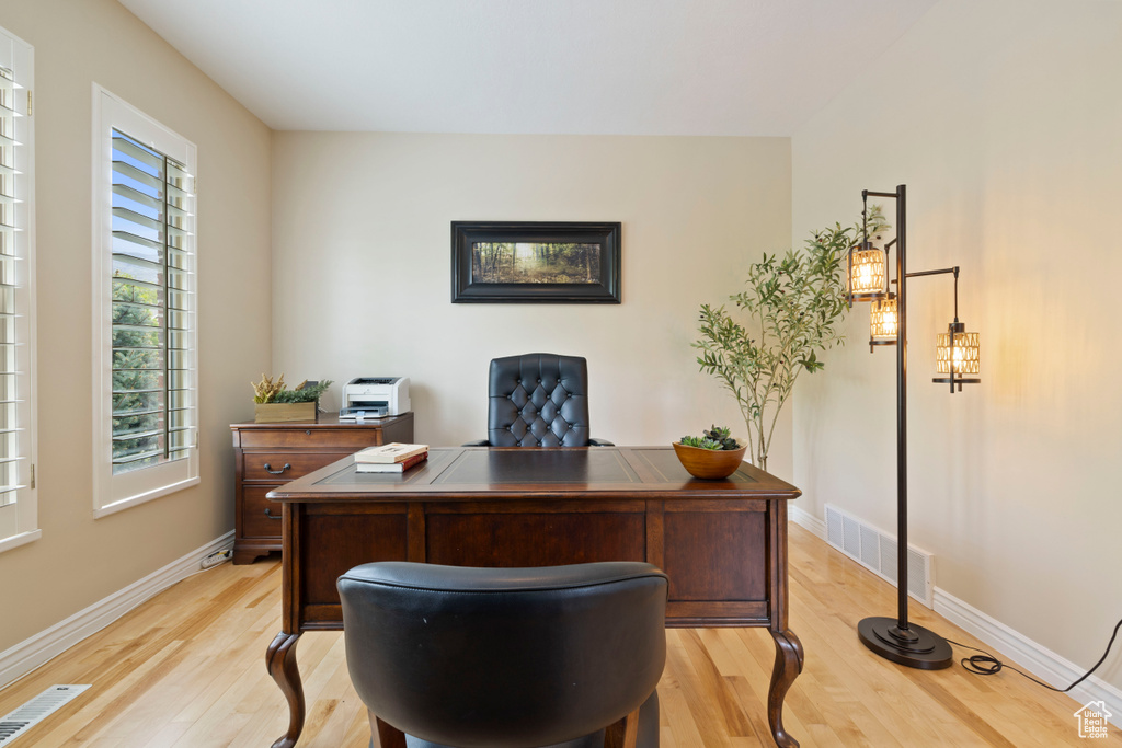 Home office with light wood-style floors, visible vents, and baseboards