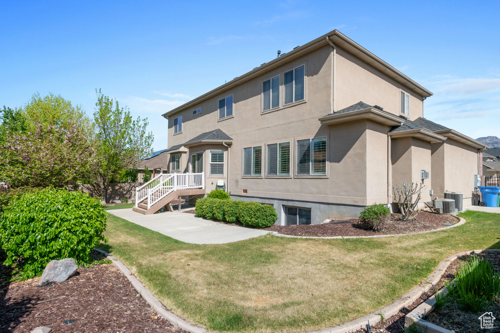 Back of house with stucco siding, a yard, and central AC