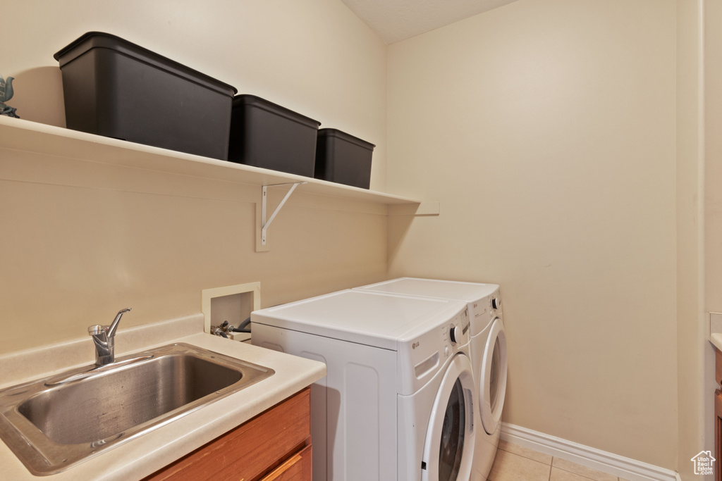 Clothes washing area featuring independent washer and dryer, cabinet space, a sink, light tile patterned floors, and baseboards