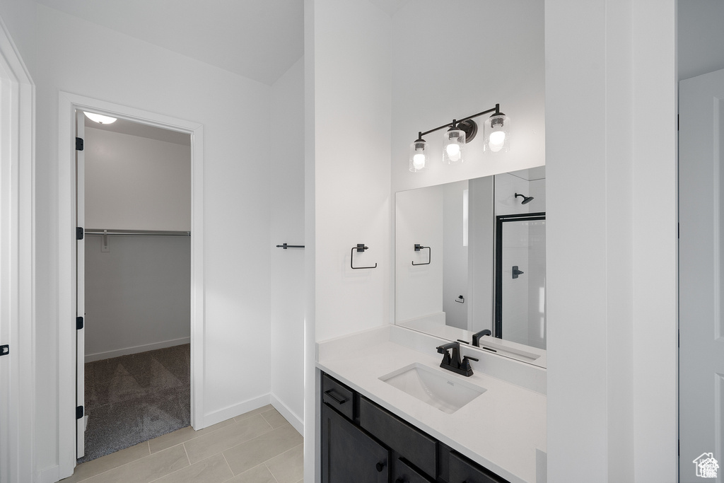 Bathroom featuring a walk in closet, vanity, tile patterned floors, baseboards, and a shower stall