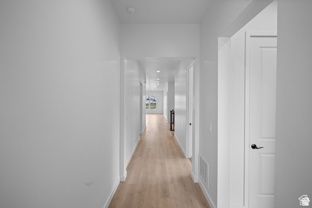 Hallway with visible vents, baseboards, and light wood-type flooring