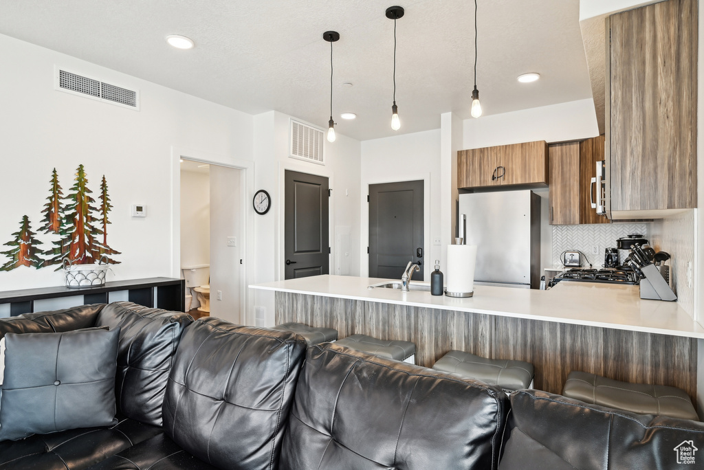 Kitchen featuring brown cabinetry, visible vents, appliances with stainless steel finishes, a peninsula, and open floor plan