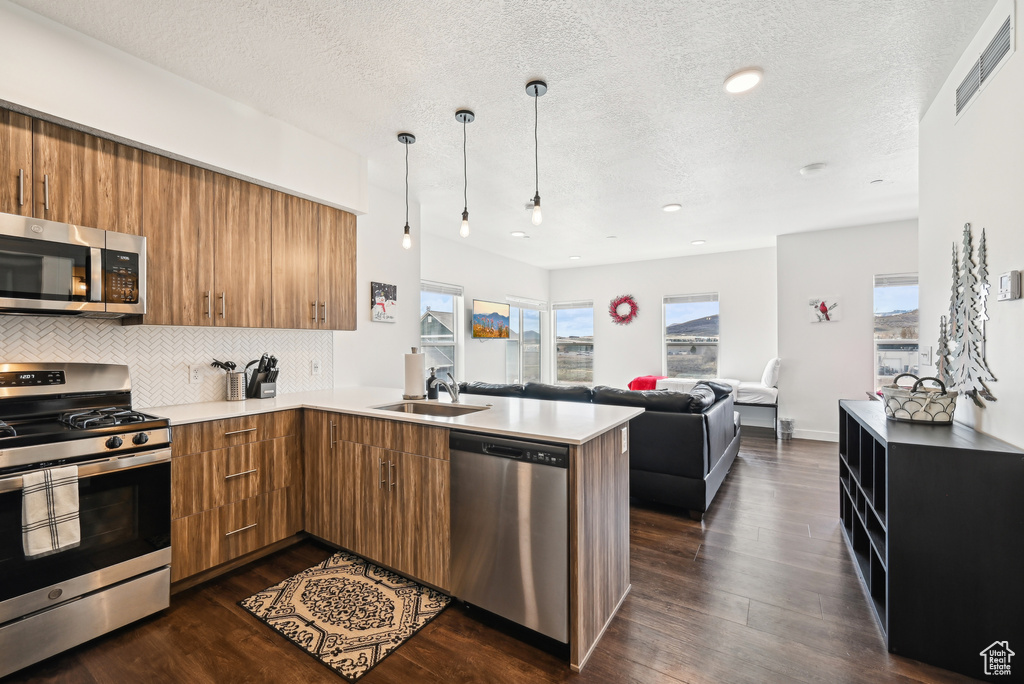 Kitchen with stainless steel appliances, a textured ceiling, and brown cabinetry