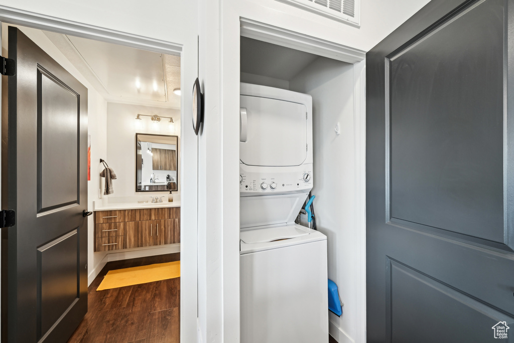 Clothes washing area featuring visible vents, stacked washer and dryer, laundry area, dark wood-type flooring, and a sink