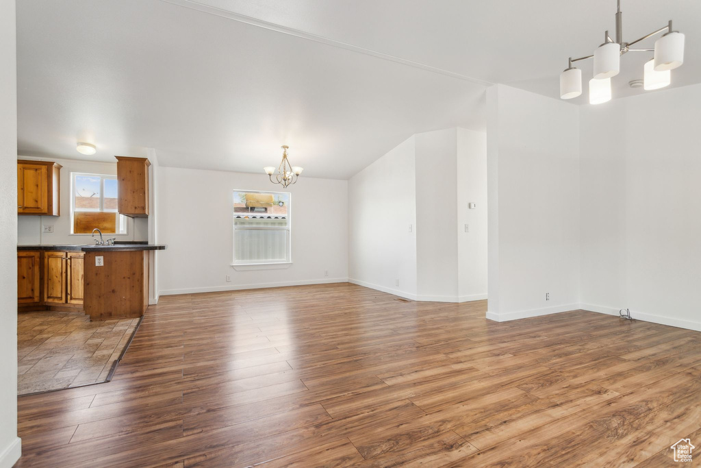 Unfurnished living room featuring a healthy amount of sunlight, baseboards, wood finished floors, and a notable chandelier