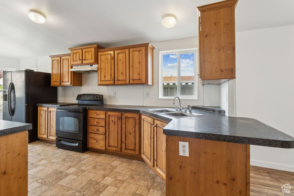 Kitchen featuring a peninsula, dark countertops, under cabinet range hood, black electric range, and a sink