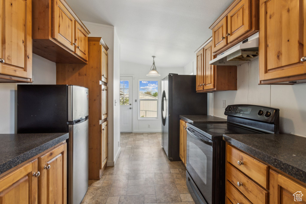 Kitchen with stone finish floor, brown cabinetry, dark countertops, black appliances, and under cabinet range hood
