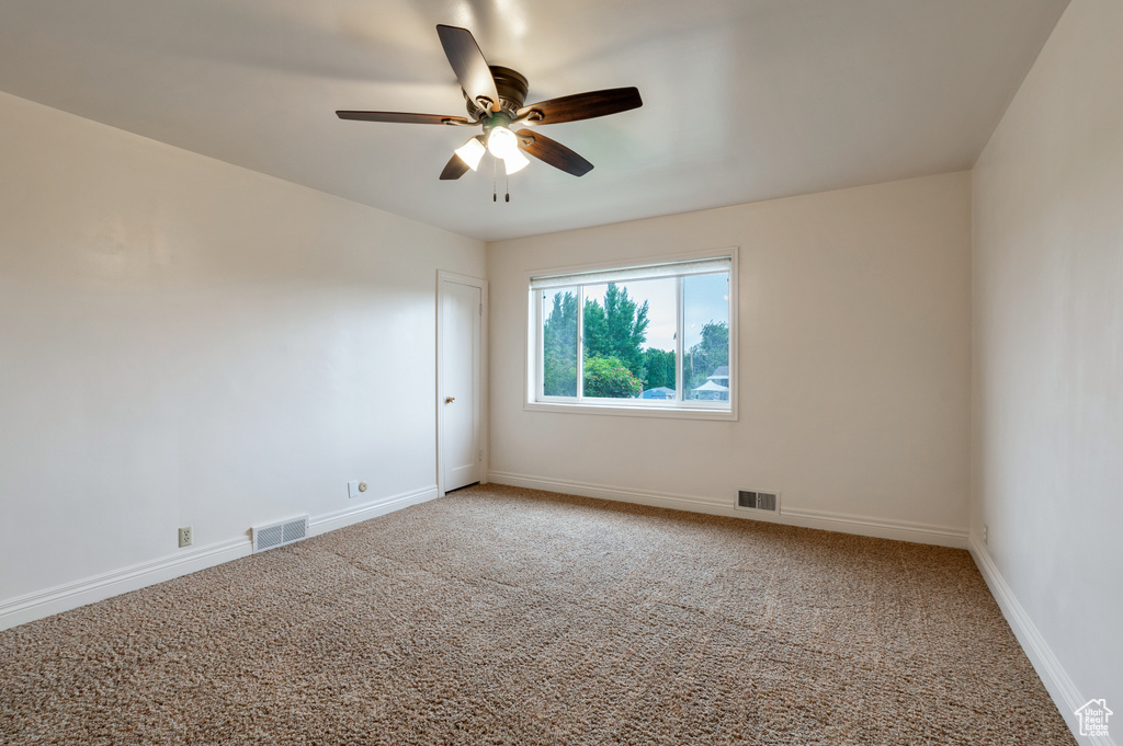 Empty room with a ceiling fan, light colored carpet, and visible vents