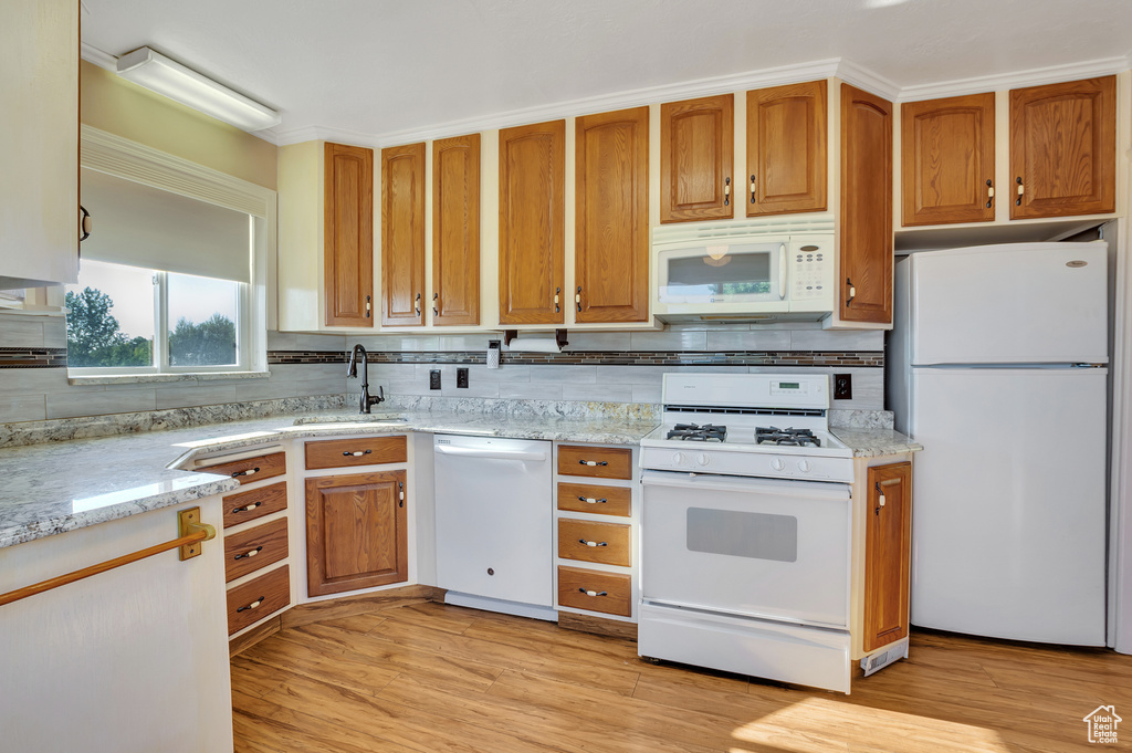 Kitchen featuring white appliances, light stone countertops, decorative backsplash, and a sink