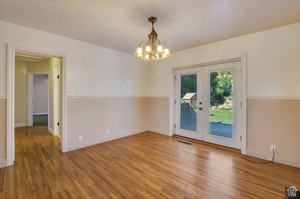 Empty room with a chandelier, french doors, visible vents, and wood finished floors